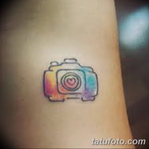 Фото тату маленького акварельного фотоаппарата с сердцем внутри объектива на запястье. Нежный и романтичный рисунок татуировки.