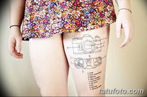 Фото тату схематичного изображения фотоаппарата на бедре. Черно-белый рисунок татуировки в стиле графики.