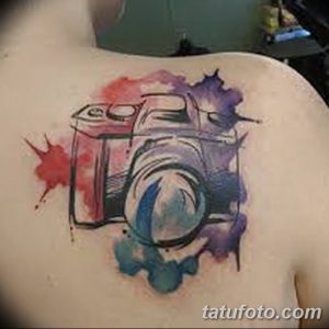 Фото тату акварельного рисунка фотоаппарата на спине. Размытые цвета и эффект брызг краски.