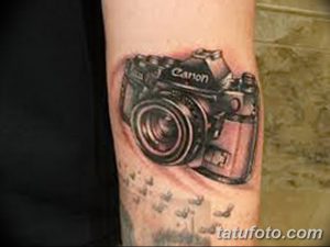 Фото реалистичной татуировки фотоаппарата Canon на предплечье. Детализированный черно-серый рисунок татуировки, имитирующий настоящий фотоаппарат.