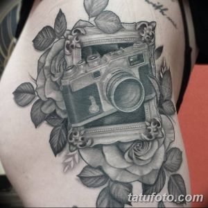 Фото тату старинного фотоаппарата, окруженного пышными розами, выполненного в чёрно-белой гамме на плече. Детализированный рисунок с реалистичными тенями.
