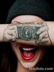 Фото тату реалистичных рук, держащих старинный фотоаппарат на руке. Изображение выполнено в черно-белом стиле, с акцентом на детали.