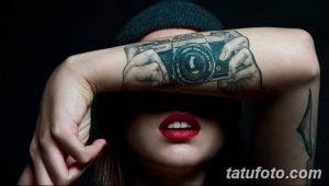 Фото тату реалистичных рук, держащих старинный фотоаппарат на руке. Изображение выполнено в черно-белом стиле.
