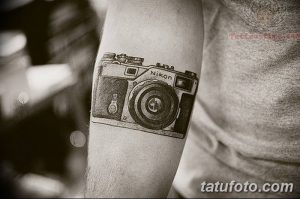 Простая татуировка камеры Nikon на руке. Черно-белый рисунок, выполненный в минималистичном стиле. Идеально для любителей бренда.