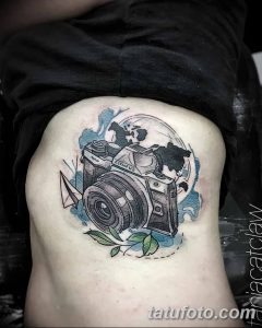 Фото тату на боку с изображением винтажной камеры Olympus, окруженной картой мира и бумажным самолетиком. Детализированный рисунок в стиле реализм.