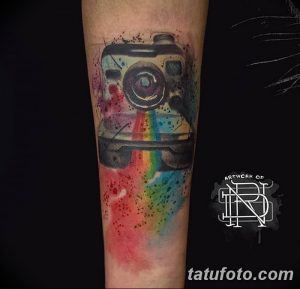 Фото акварельной татуировки фотоаппарата с радугой на руке. Яркий и красочный рисунок с размытыми краями.