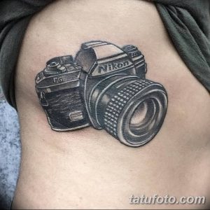 Фото тату реалистичного фотоаппарата Nikon на плече. Черно-белый рисунок с высокой детализацией, имитирующий фотографию.