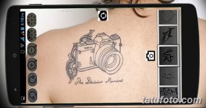 Фото эскиза татуировки фотоаппарата, нанесенного на плечо. Изображение выполнено в черно-белом цвете с использованием тонких линий и надписью "The Decisive Moment".