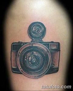 Фото тату реалистичного изображения старинного фотоаппарата с поднятым видоискателем. Татуировка выполнена в коричневых и черных тонах с проработкой деталей.