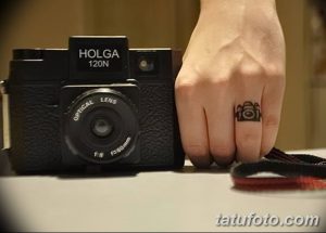 Фото тату: необычная татуировка фотоаппарата, выполненная на пальце руки, в реалистичном стиле.