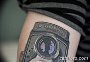 Фото тату: татуировка фотоаппарата на руке с эффектом старой пленки и винтажной цветокоррекции, выполненная в черно-серых тонах.