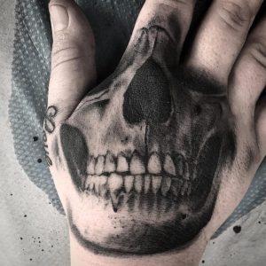 Фото тату: реалистичная татуировка черепа на руке. Детализированный рисунок татуировки в черно-серых тонах.
