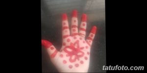 Фото тату хной на ладони с изображением цветка и точек. Простой и минималистичный рисунок в красных тонах.