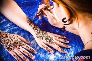 Фото процесса нанесения тату мехенди на руку, мастер аккуратно наносит хну с помощью специального инструмента. Детализированный рисунок с цветочными мотивами.