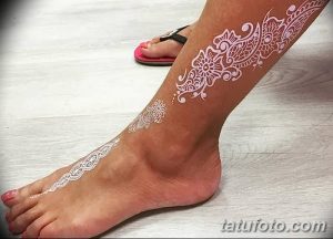 Фото тату белым мехенди на ноге. Изящные цветочные узоры и геометрические элементы создают нежный и воздушный образ.