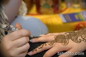 Фото процесса нанесения тату мехенди на руку, мастер аккуратно наносит узор с помощью специальной пасты. Детальный снимок для вдохновения.