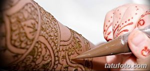 Фото процесса нанесения тату хной на руку, мастер аккуратно наносит узор с помощью специального инструмента.