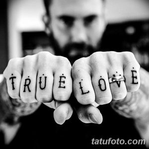 Фото тату: надпись 'TRUE LOVE' на костяшках пальцев мужчины. Черно-белая татуировка, выполненная четким шрифтом. Идея для тату.