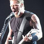 Фотография Джеймса Хетфилда из Metallica, выступающего на сцене с микрофоном. Видны татуировки на его руках и плечах.