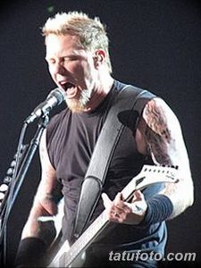 Фотография Джеймса Хетфилда из Metallica, выступающего на сцене с микрофоном. Видны татуировки на его руках и плечах.