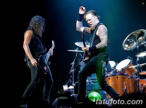 Фотография Джеймса Хетфилда и Кирка Хэмметта из Metallica во время энергичного живого выступления на сцене. Видны татуировки на руках Джеймса Хетфилда.