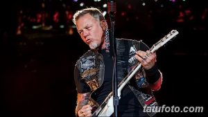 Фотография Джеймса Хетфилда, лидера Metallica, играющего на гитаре на сцене, демонстрирующая его многочисленные татуировки на руках.