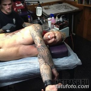 Фотография Джеймса Хетфилда во время сеанса татуировки. Видны татуировки на его руках и плечах, а также тату-мастер, работающий над рисунком.