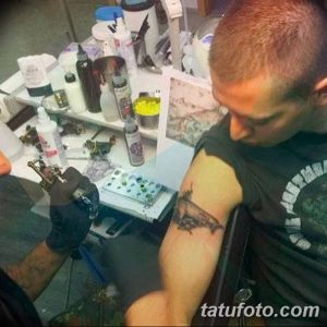 Фото процесса нанесения татуировки на руку мужчины. Мастер тату работает над рисунком, используя специальное оборудование и инструменты.