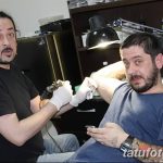 Фотография мастера тату, работающего над татуировкой на руке клиента. Видно тату-машинка, рука клиента и мастер в процессе нанесения рисунка.