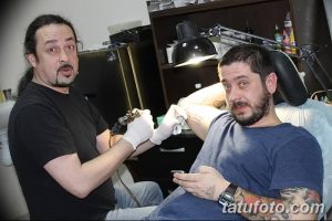 Фотография мастера тату, работающего над татуировкой на руке клиента. Видно тату-машинка, рука клиента и мастер в процессе нанесения рисунка.