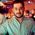 Фотография мужчины с татуировкой на руке, выполненной в ярких цветах. Татуировка изображает сложные узоры и детали, заметные на фоне размытого фона.