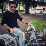 Фото мужчины с татуировкой на руке, сидящего на велосипеде в парке. Видны детали татуировки на предплечье.