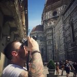 Фото мужчины с татуировкой на руке, фотографирующего собор в Италии. Видны детали татуировки на предплечье и плече.