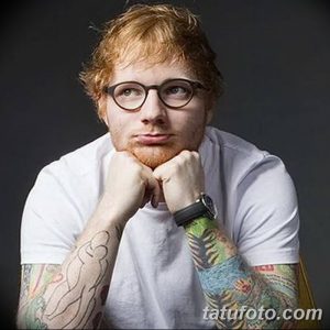 Фотография Эда Ширана с татуированными руками, демонстрирующая его задумчивый взгляд и повседневный стиль.