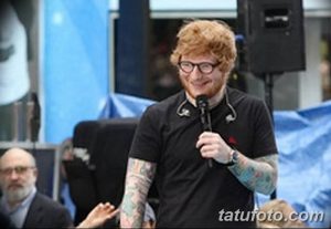 Фотография Эда Ширана во время выступления, демонстрирующая его татуированные руки и микрофон.