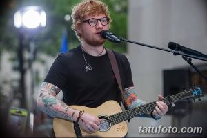 Фотография Эда Ширана с гитарой, демонстрирующая его татуированные руки и повседневный стиль.