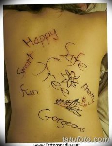 Фото тату хной на спине девушки с надписями 'Happy', 'Smart', 'Safe', 'Free', 'Fun', 'Gorgeous' и изображением цветка.