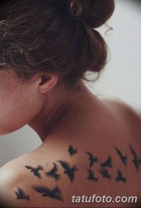 Фото минималистичной татуировки на лопатке, изображающей стаю летящих птиц. Выполнена в черном цвете, с акцентом на легкость и свободу.