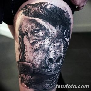 Фото татуировки, изображающей ворона, сидящего на плече у викинга с бородой и шлемом. Рисунок выполнен в черно-серой гамме с высокой детализацией.