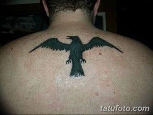 Черно-белая татуировка с изображением ворона в полете, с широко распахнутыми крыльями. Рисунок выполнен в минималистичном стиле, с акцентом на силуэт птицы.