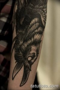 Фото тату ворона на руке мужчины. Рисунок выполнен в черно-серой гамме с использованием техники дотворк.