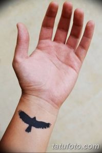Фото минималистичного тату ворона в полете на запястье. Простой, но выразительный рисунок в черном цвете.