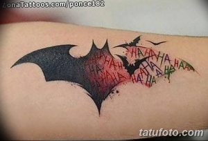 Фото тату Бэтмена и Джокера на руке, выполненное в ярких цветах с использованием элементов граффити и надписей "HAHAHA". Динамичный и хаотичный рисунок.