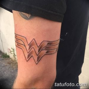 Фото тату: Золотой символ Wonder Woman на предплечье, выполненный в контурном стиле с добавлением теней.