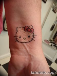 Черно-белое фото татуировки на запястье с изображением Hello Kitty, выполненной в классическом стиле с использованием четких линий и ярких цветов.