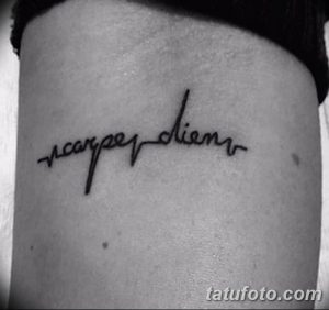 Фото тату: небольшая, черная татуировка с надписью 'Carpe Diem' на руке, выполненная каллиграфическим шрифтом.