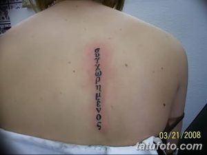 Фотография татуировки на спине, представляющей собой надпись на греческом языке, выполненную черными чернилами.