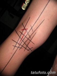 Фотография минималистичной татуировки на предплечье, состоящей из пересекающихся черных линий и нескольких красных акцентов. Стиль - графика.