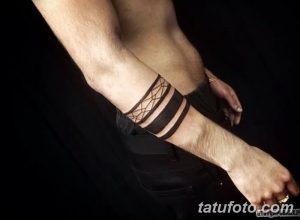 Фото тату: татуировка в виде браслета на запястье мужчины, состоящая из черных полос и геометрического узора.