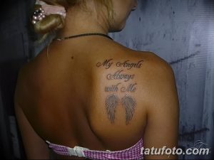 Фото тату надписи 'My Angels Always With Me' на лопатке, с изображением крыльев. Черно-серые тона, реалистичные крылья, нежный дизайн.